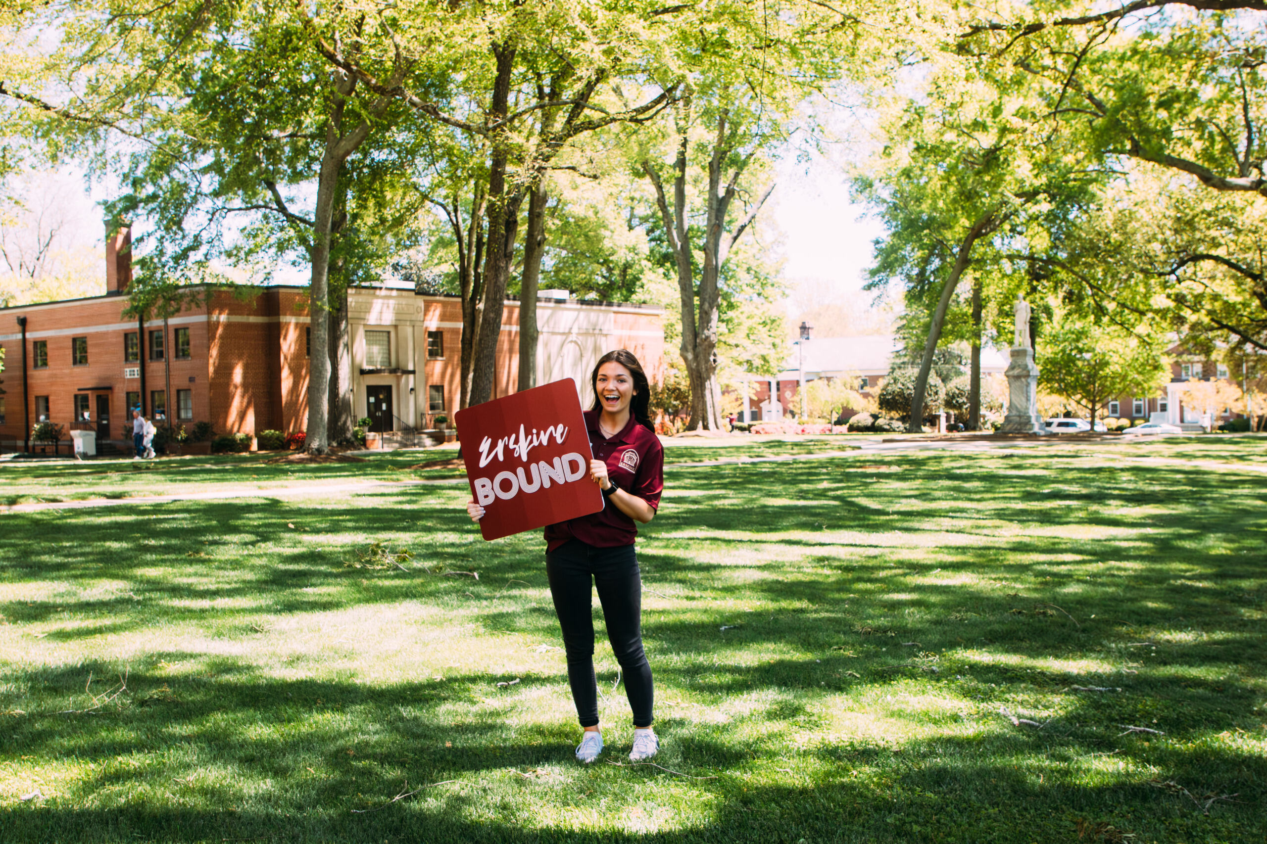 Erskine Student stands under the towers holding an "Erskine Bound" sign