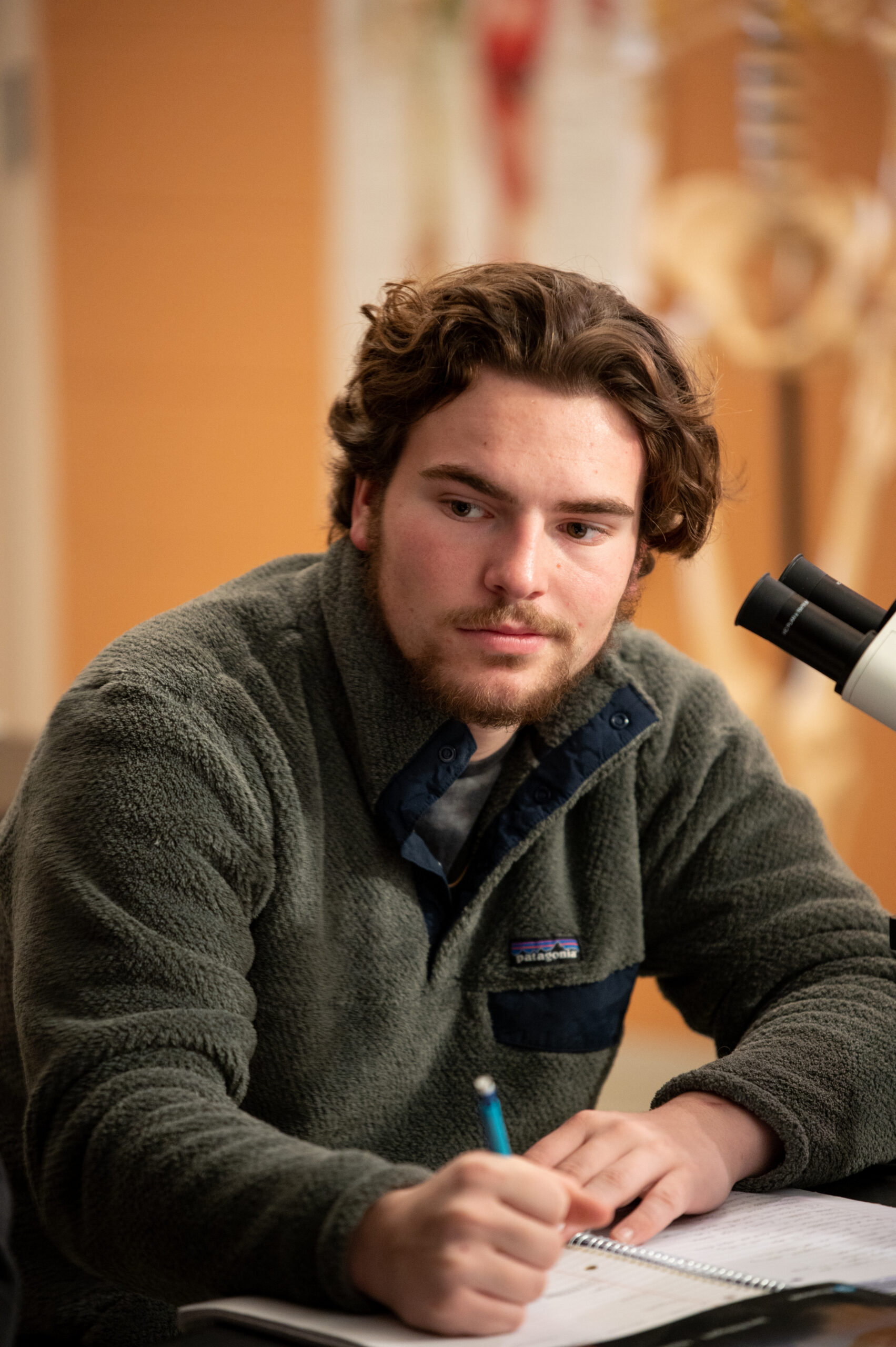 A student takes notes beside a microscope
